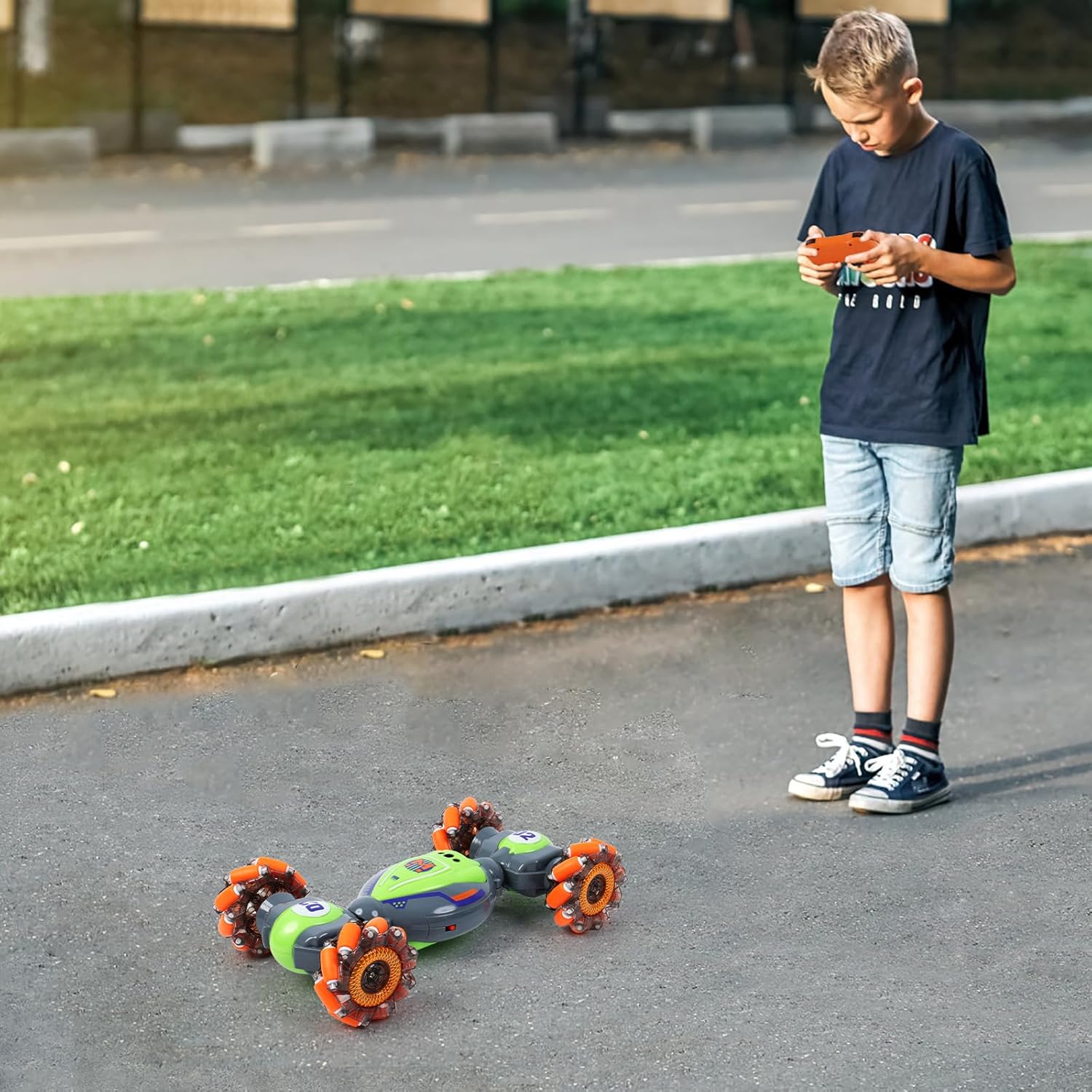 Young boy playing with the QXHOL green and orange stunt car using a remote controller on an outdoor pavement.